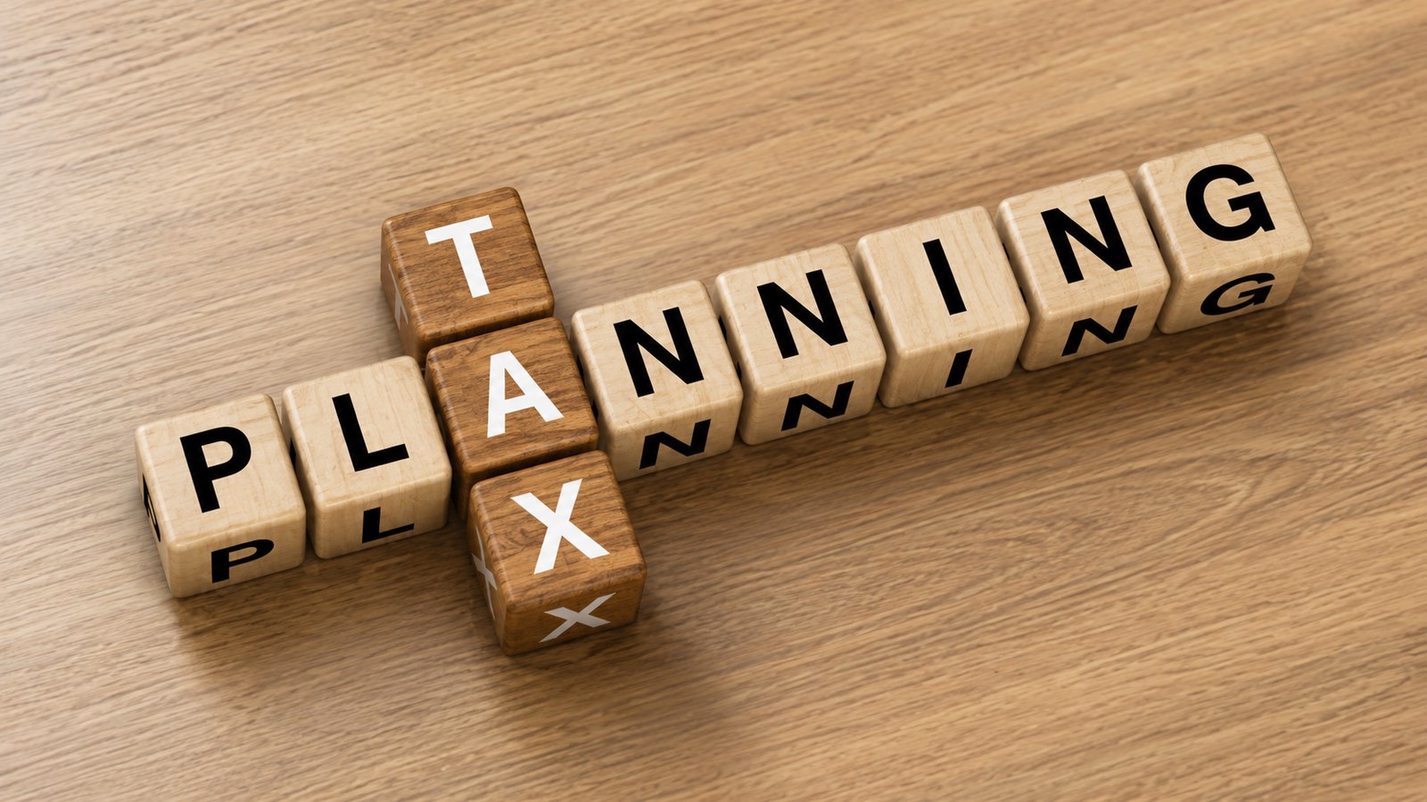 Wooden letter blocks spelling tax planning as a crossword on a timber desk